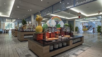 Un hall amplio con una zona de buffet central que ofrece diversas opciones de comida y elementos decorativos como una escultura de jirafa y un arcoíris.