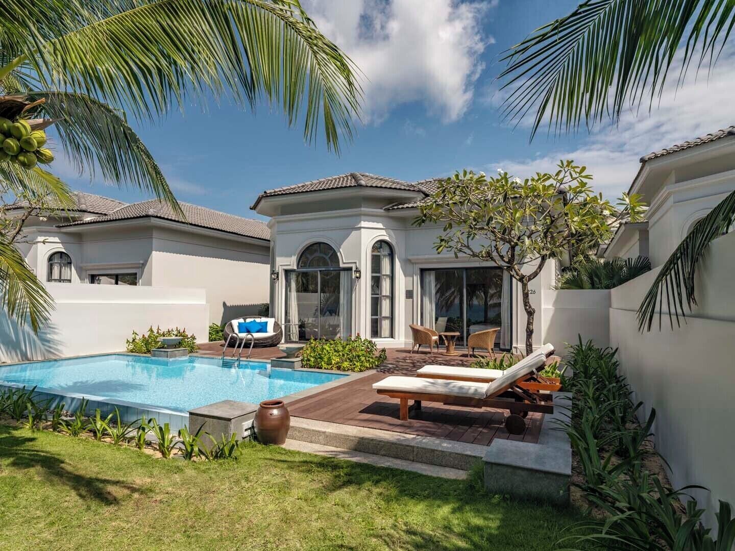 A poolside area with a clear blue pool, lounge chairs, and a small seating area with a table and chairs.