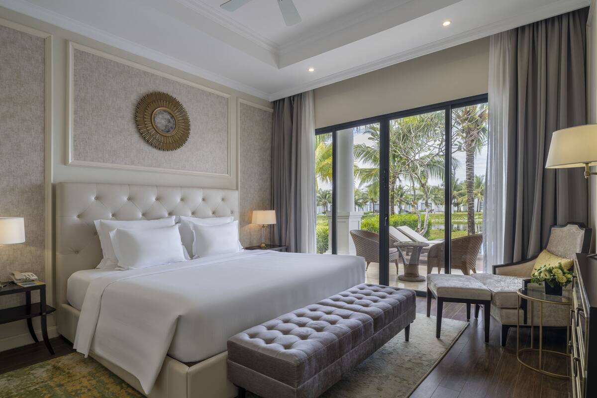 Ruime hotelkamer met een groot bed, een zithoek met uitzicht op palmbomen en een balkon.