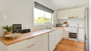 Une cuisine moderne avec des armoires blanches, un plan de travail en bois, un lave-vaisselle encastré, une cuisinière et un réfrigérateur.