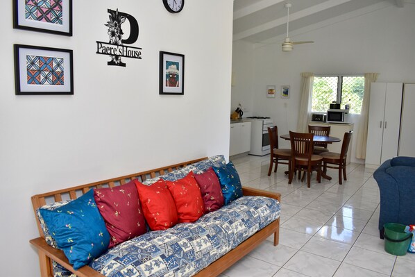 A living room with a sofa, a dining area with a table and chairs, a kitchen area with a microwave, and a ceiling fan. - Paere House, Snorkeling Heaven (Tikioki Beach)