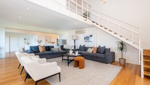 A spacious living room with a grey sofa set, a coffee table, and a staircase. - Pet Friendly - Bay Views From Drury Lane with Solar Heated Pool and Gas Heated Spa (Dromana)