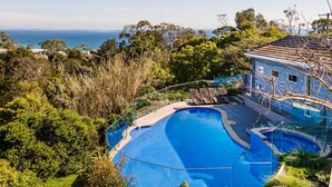 A pool with a curved edge, surrounded by lush greenery and overlooking a coastal view. - Pet Friendly - Bay Views From Drury Lane with Solar Heated Pool and Gas Heated Spa (Dromana)