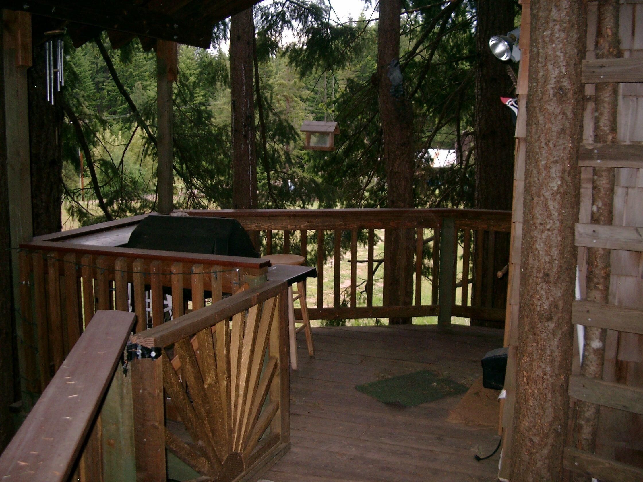 A wooden deck with a grill and seating area, surrounded by trees.