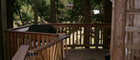 A wooden deck with a grill and seating area, surrounded by trees.