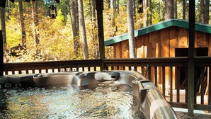 Een hottub omgeven door een houten terras, met uitzicht op een bos.