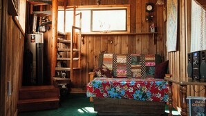 Een knus interieur van een blokhut met een houten vloer, een bed met een bloemenprint, een houten ladder, een kachel en een raam met uitzicht.