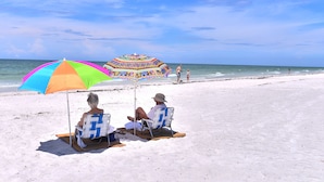 Two people sitting under a colorful beach umbrella on a sandy beach with a clear sky. - Direct Gulf Front Beach Paradise! Any Closer To The Water & You Would Be In It.. (Indian Shores)