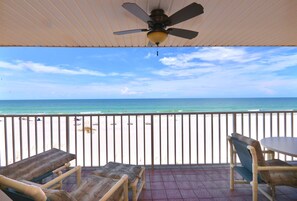 Un espace extérieur abrité, doté d’un ventilateur de plafond, d’une table et de deux fauteuils. Il offre une vue sur une plage, avec une rambarde, et sur l’océan.