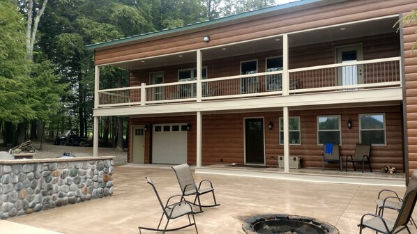 A two-story log cabin with a balcony, stone wall, and outdoor seating area.