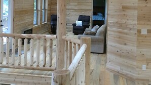 Een houten blokhut van binnen met een balkon, een bank en een bed.
