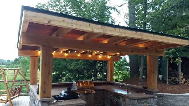 Een buitenkeuken met een stenen aanrecht, een barbecue en een pergola met lichtslingers.