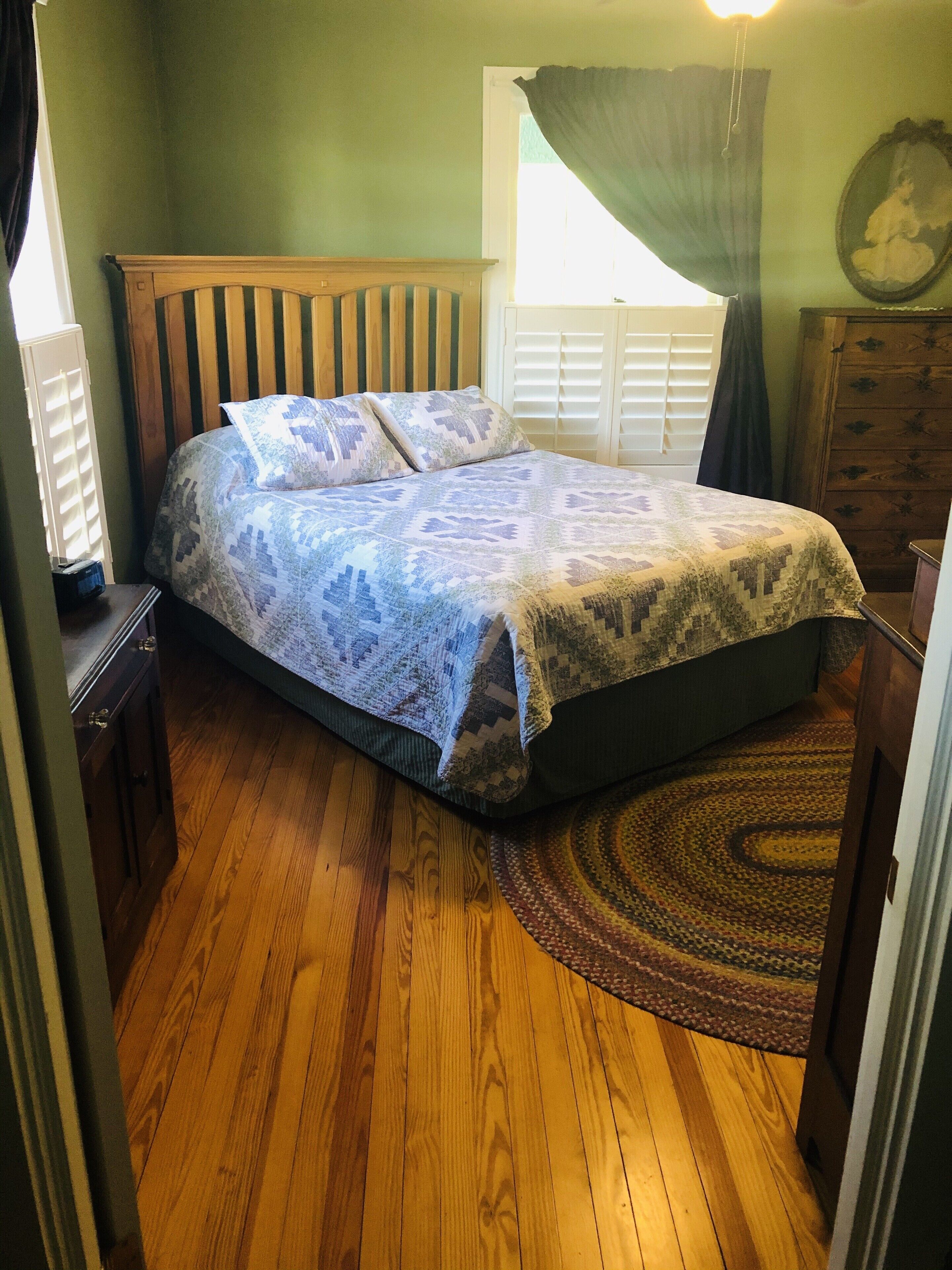 A bedroom with a wooden bed, a window with curtains, a wooden dresser, and a patterned rug.