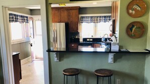 Una cocina con armarios de madera, un refrigerador de acero inoxidable, una encimera negra y dos taburetes.