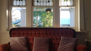 Habitación con cabecera tapizada en rojo, dos almohadas y vistas a través de tres ventanas con una lámpara colgante.