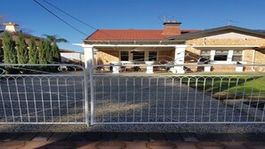 Una propiedad residencial con entrada protegida por un muro, un porche cubierto y una casa de ladrillo con techo rojo.