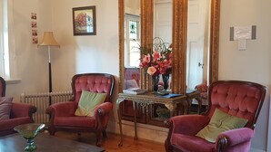 Una habitación con dos sillones tapizados en rojo, una mesita con un florero y un radiador, además de un espejo.
