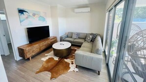 Ein modernes Wohnzimmer mit Flachbildfernseher, einer Holz-Unterhaltungsecke, einem runden Couchtisch, einem grauen Sofa und einem Kuhfellteppich.