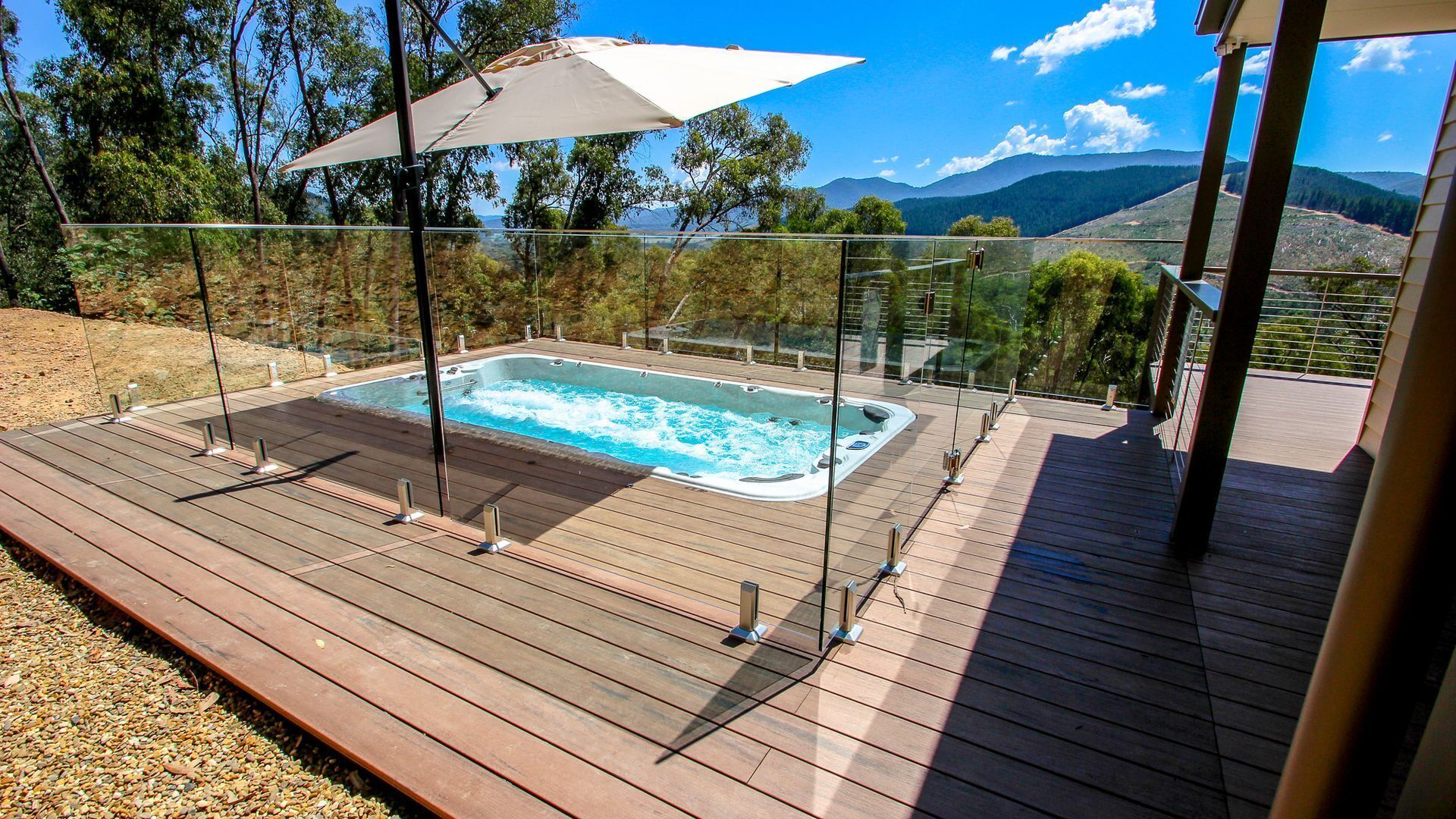 Um deck de madeira com hidromassagem, guarda-corpo de vidro e vista para montanhas.