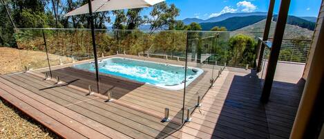 Um deck de madeira com hidromassagem, guarda-corpo de vidro e vista para montanhas.
