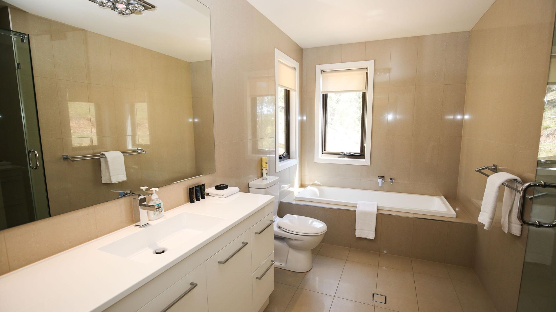 A modern bathroom with a large mirror, a bathtub, a toilet, and a sink.