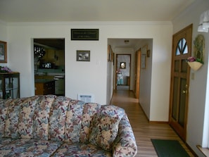 A living room with a floral sofa, a kitchen in the background, and a hallway leading to a door.