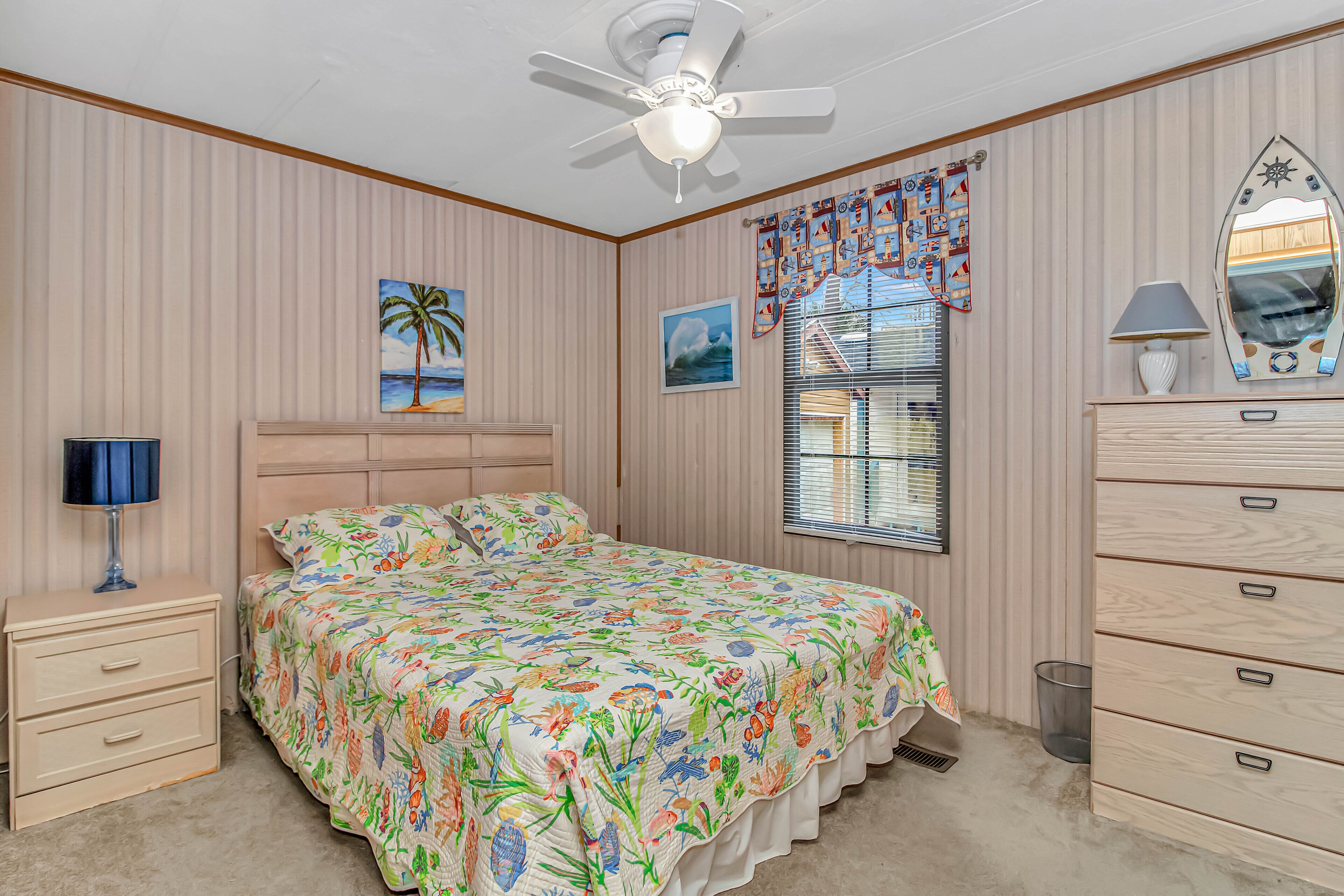 A bedroom with a bed, a nightstand, a dresser, a ceiling fan, and a window with blinds.