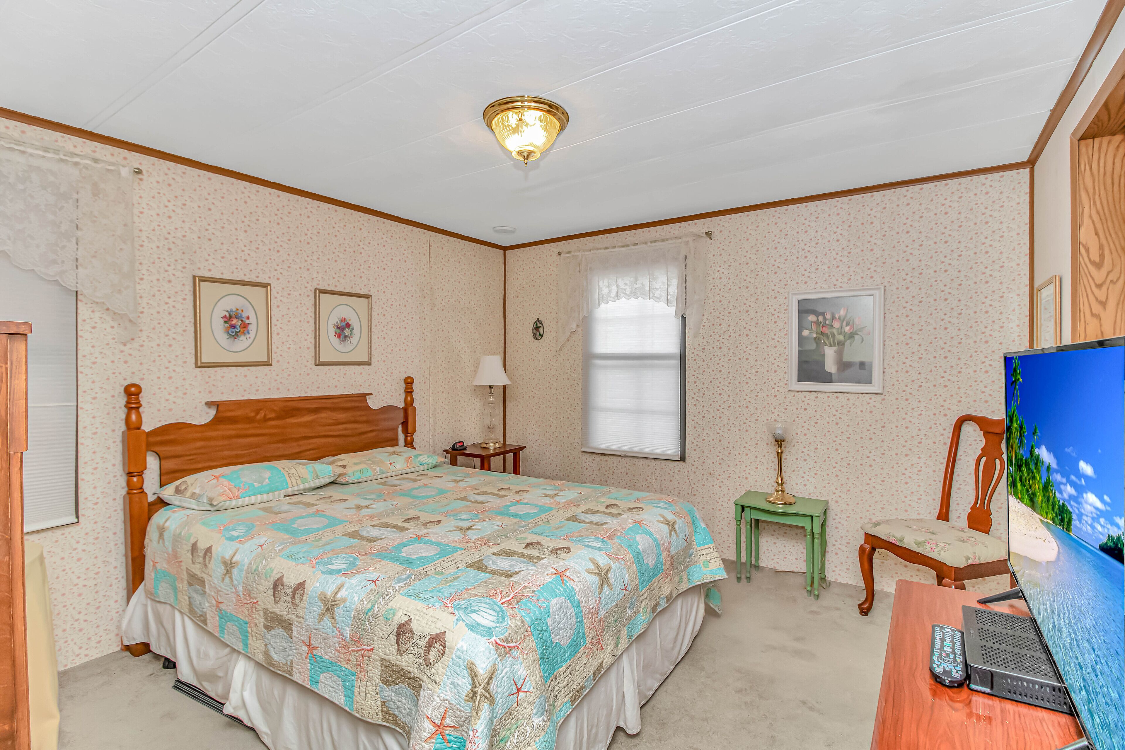 Ein Schlafzimmer mit einem hölzernen Bett, einem Schreibtisch mit Computer, einem Fernseher und einem kleinen Tisch mit Lampe.