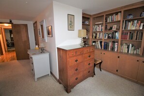 Um quarto com um armário de madeira, uma cômoda branca e uma estante repleta de livros.