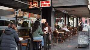 Un área de estar al aire libre con mesas y sillas, un letrero que indica 'WINE FOOD' y un letrero de 'WILLING BROS. WINE MERCHANTS ABIERTO 7:30 AM'.