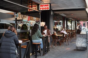 Un restaurante con terraza, un letrero que indica vino y comida, y un cartel para los comerciantes de vino Willing Bros.