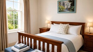 Un dormitorio con cama de madera, dos mesitas de noche, un ventanal con cortinas y un cuadro en la pared.