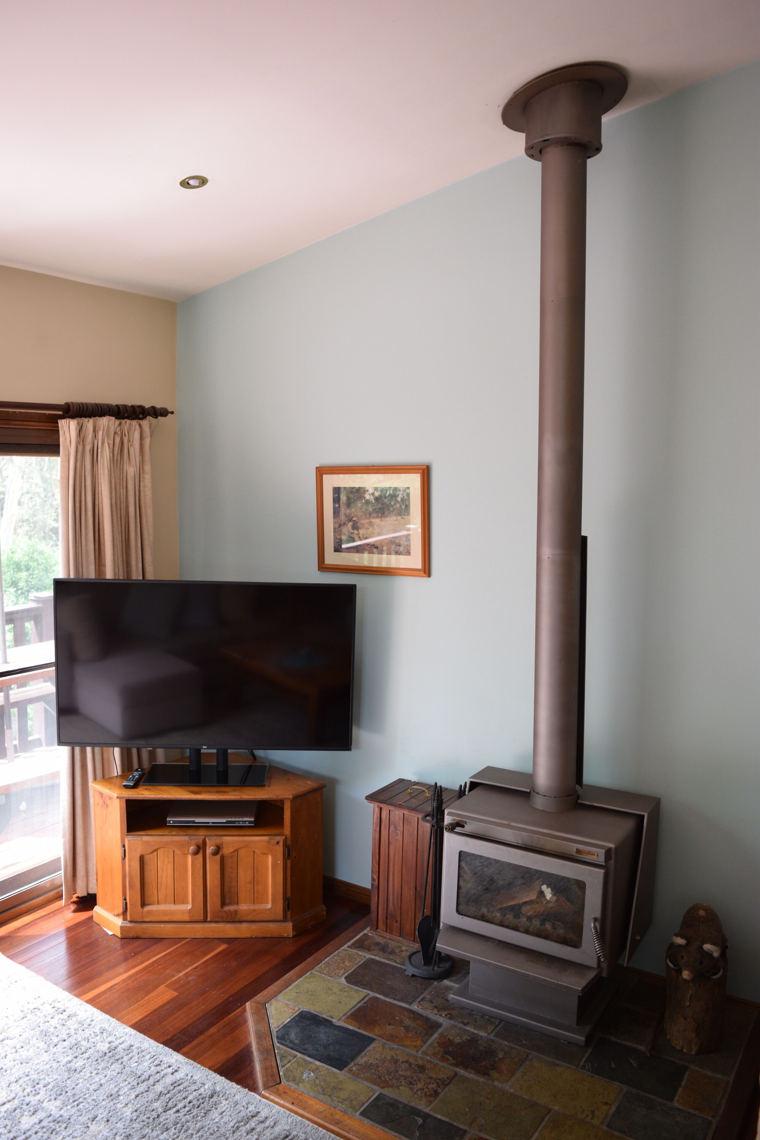 A living room with a television on a wooden stand, a stone fireplace, and a window with curtains.