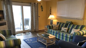 A living room with a striped sofa, a blue armchair, a coffee table, and a lamp. - Oceanfront 1BR/2BR Condo on 2nd Floor, 1,000 SQ FT (Panama City Beach)