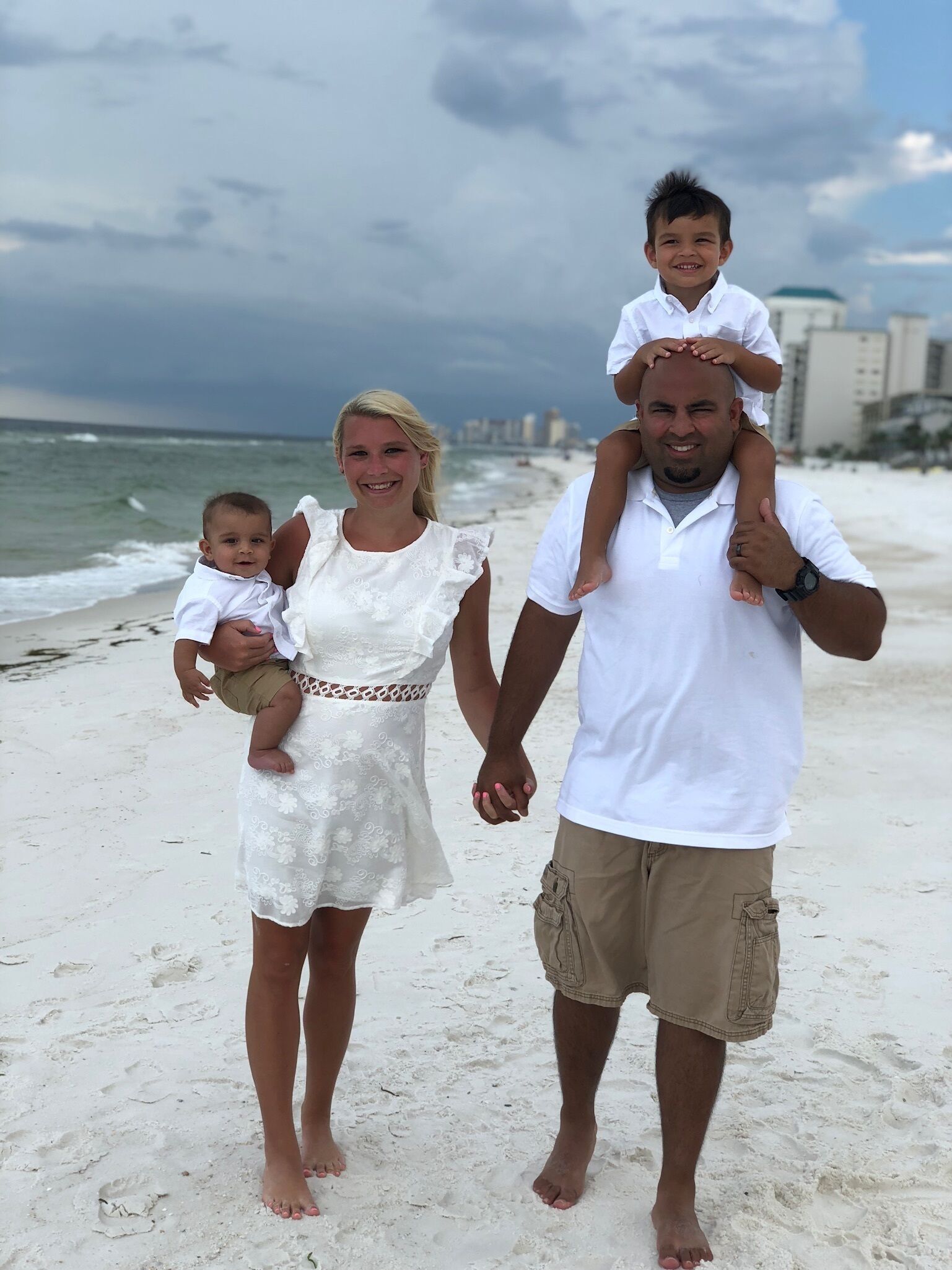 A family on a beach with a man carrying a child on his shoulders and another child in his arms.