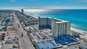 An aerial view of a coastal hotel with a parking lot, beachfront, and a large building with multiple floors. - Oceanfront 1BR/2BR Condo on 2nd Floor, 1,000 SQ FT (Panama City Beach)
