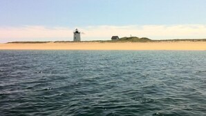 Ein Leuchtturm an einem sandigen Strand, im Vordergrund ruhiges Wasser.