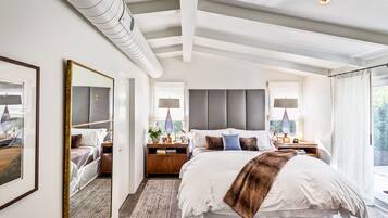 A modern bedroom with a large bed, bedside tables, a mirror, and a view of greenery outside.