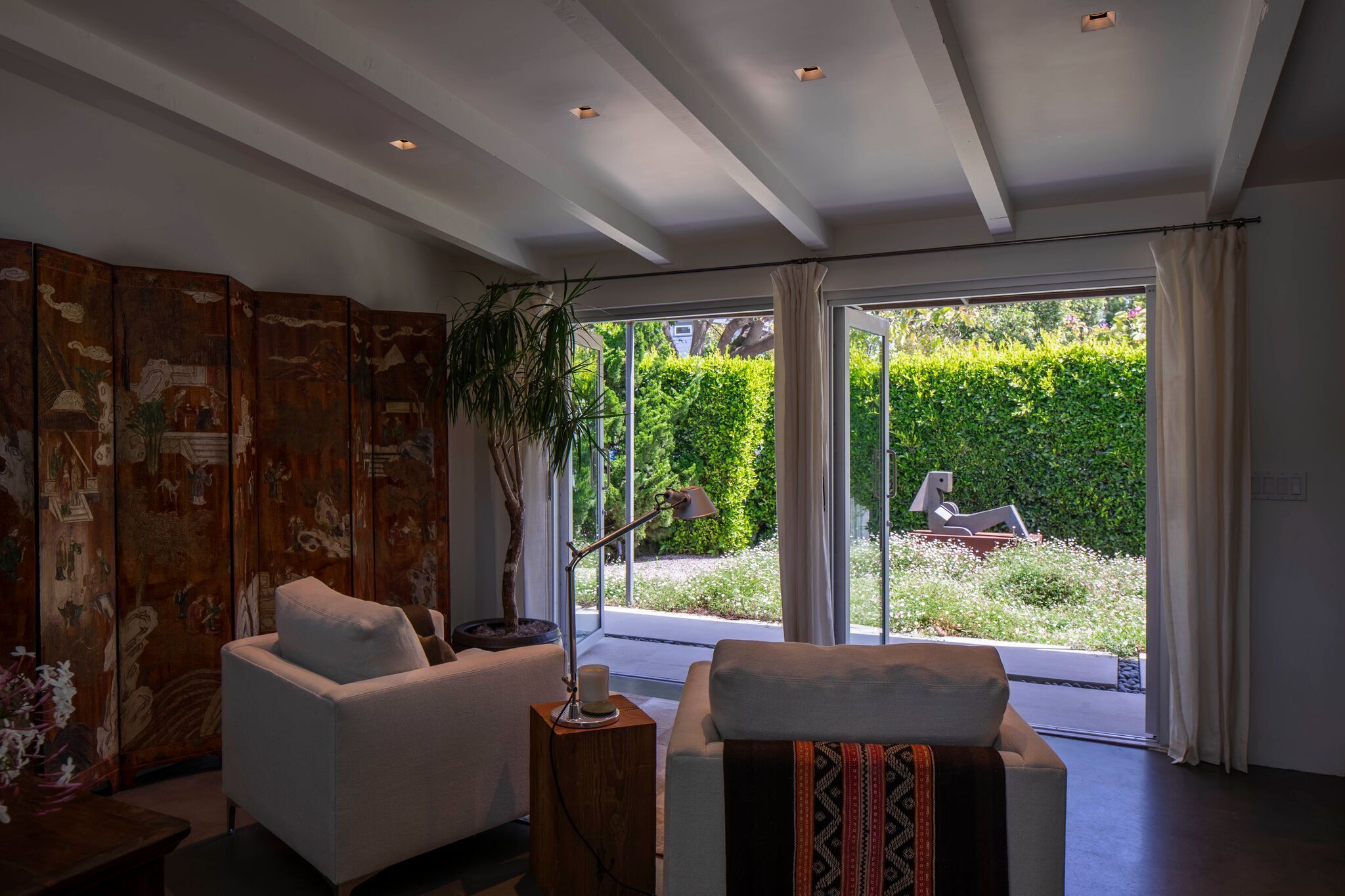 A modern living room with a sofa, a side table, and a large window with a view of a garden.
