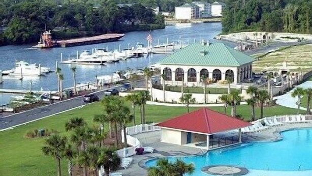 A large swimming pool with a red-roofed pavilion, surrounded by palm trees and a marina with boats. - BEAUTIFUL 2BR condo;Norman Course, Barefoot Resort;top-rated beach! (North Myrtle Beach)