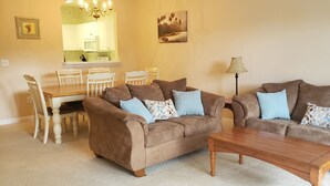 A living room with two brown sofas, a wooden coffee table, and a dining area with a white table and chairs. - BEAUTIFUL 2BR condo;Norman Course, Barefoot Resort;top-rated beach! (North Myrtle Beach)