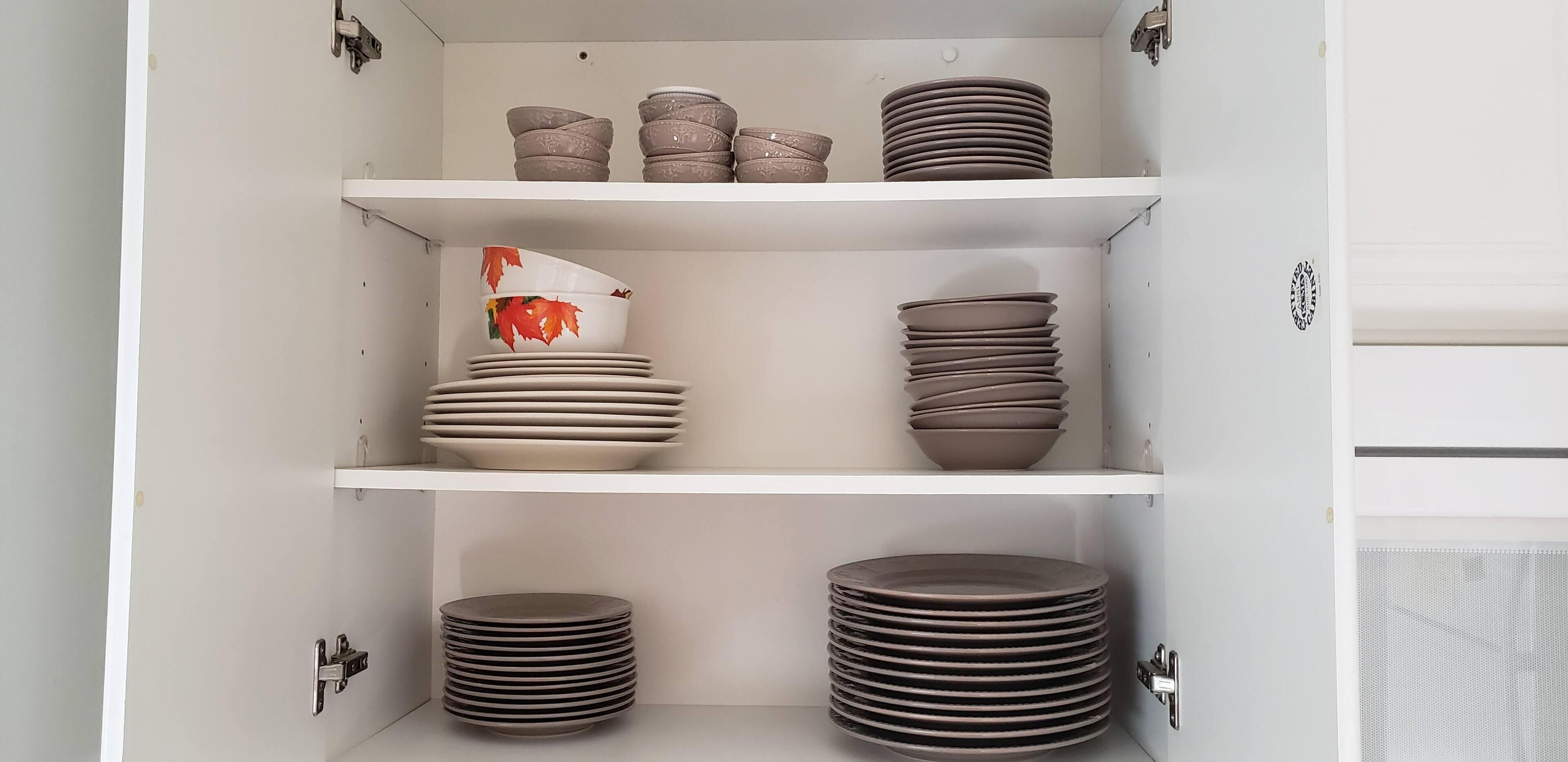 A cabinet with three shelves, each holding stacks of plates and bowls.