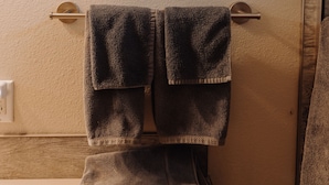 Une salle de bain avec un tableau représentant un paysage, un porte-serviettes avec deux serviettes et une porte en bois.