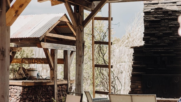 Une terrasse extérieure aménagée avec du mobilier en bois, une cheminée en pierre et une vue sur le paysage environnant.