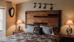 Une chambre à coucher avec une tête de lit en bois, une couvre-lit à motifs, deux lampes de chevet et un miroir fixé au mur.
