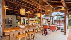 Amplio espacio interior con techo de madera, zona de bar con taburetes y área de estar con sofás y sillones.