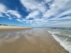 Una spiaggia con un'ampia distesa di sabbia, cielo sereno con nuvole sparse e mare calmo.
