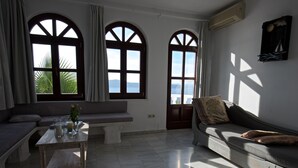 A living room with a sofa, a bench, and a table with candles. There are three arched windows with curtains. - Breathtaking view, luxury, privacy, style and much more ! (Firostefani)