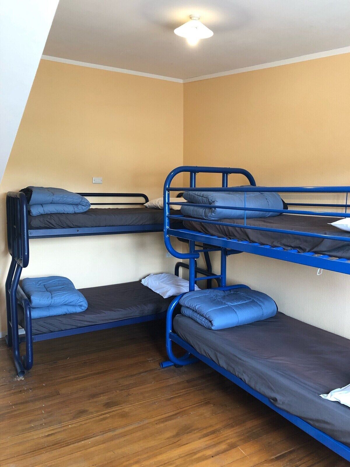 A dormitory room with bunk beds, wooden flooring, and a ceiling light fixture.