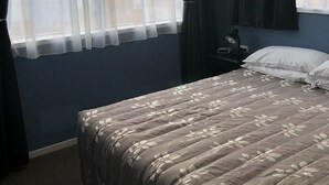 A bedroom with a bed, a nightstand, a lamp, and a window with curtains. - The heart of Ohakune township with mountain views (Ohakune)